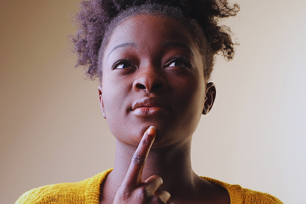 African woman thoughtfully resting her finger on her chin, reflecting on concerns and questions related to a possible NIPT false positive result during pregnancy screening.