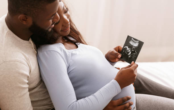 Relaxed african couple watching baby ultrasound photo, lying in bed at home, free space learning about NIPT vs FTS