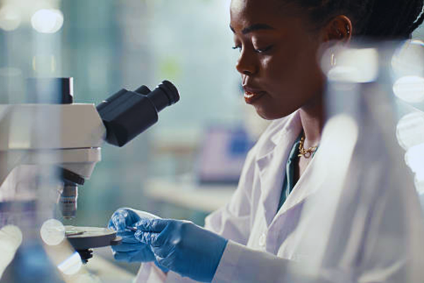 A photorealistic image of a black woman using a microscope in a biotechnology laboratory, conducting research and DNA analysis, representing the process of DNA paternity testing through scientific and forensic examination.