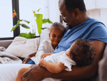 Beyond Doubt Understanding and Overcoming the Stigma of Misattributed Paternity Man holding his daughters in his arms, symbolizing family bonds while highlighting emotional and legal concerns related to misattributed paternity.