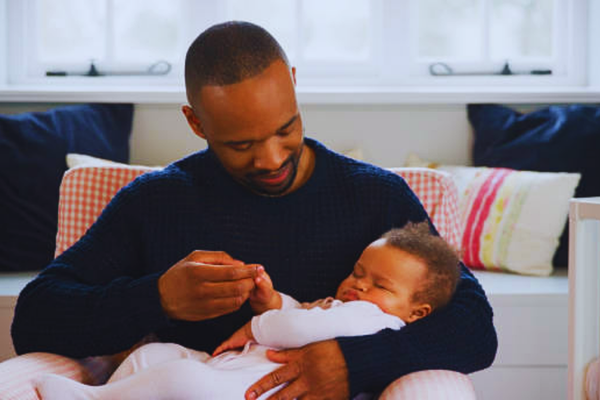 New father cuddling his sleeping baby girl in a home nursery, symbolizing family bonding and the importance of paternity testing accuracy.