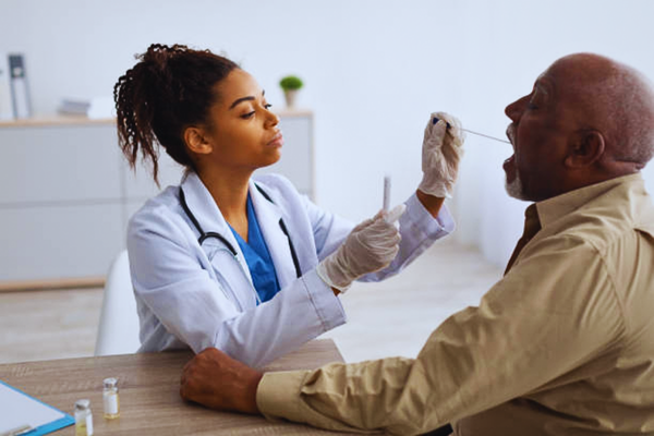 Black medical worker performing a COVID-19 PCR swab test on a mature male patient, illustrating diagnostic procedures and raising awareness about when you can get a paternity test during medical situations.